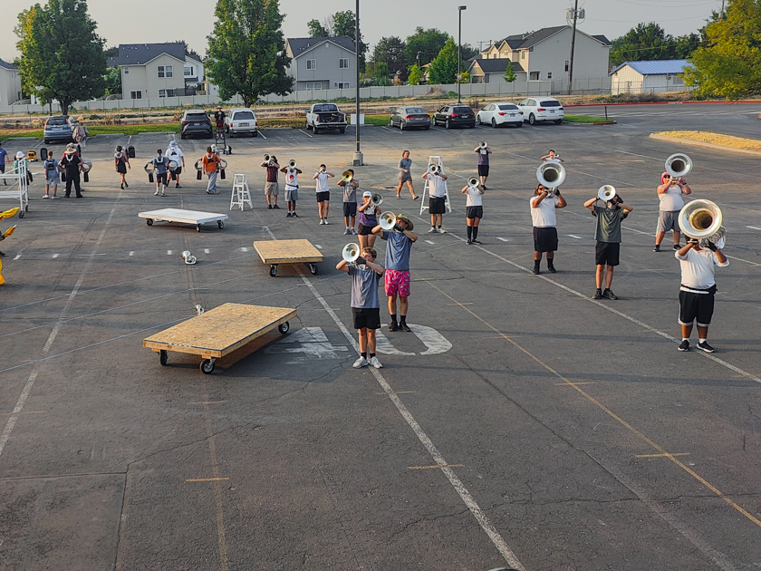 Marching band brass section rehearsing drill on a marked parking lot practice field